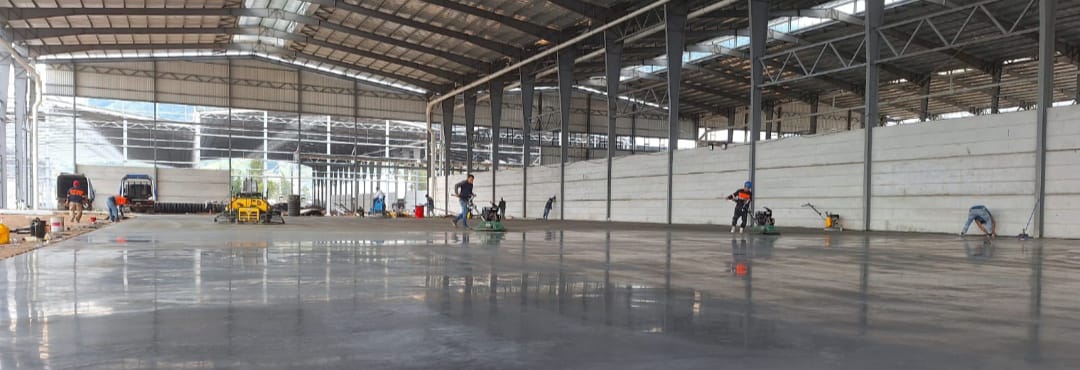 Proceso de afinado y pulido de piso industrial de concreto con allanadoras mecánicas en Bodegas Cuenca, Guatemala. Alta calidad de superficie.